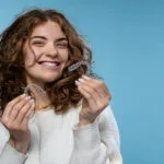A woman is holding Invisalign clear aligners and smiling